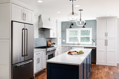 Inredning av ett klassiskt mellanstort vit vitt kök, med en undermonterad diskho, skåp i shakerstil, vita skåp, bänkskiva i kvarts, blått stänkskydd, stänkskydd i keramik, rostfria vitvaror, mellanmörkt trägolv, en köksö och brunt golv