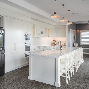 Photo of a transitional u-shaped eat-in kitchen in Sunshine Coast with a farmhouse sink, shaker cabinets, white cabinets, quartz benchtops, white splashback, subway tile splashback, stainless steel appliances, with island, grey floor and white benchtop.