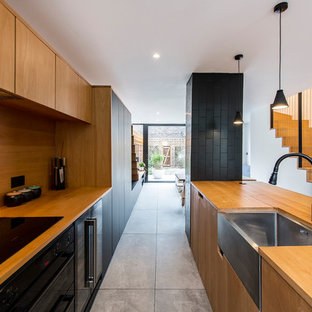 Inspiration for a scandinavian kitchen in Sussex with a belfast sink, flat-panel cabinets, medium wood cabinets, wood worktops, wood splashback, black appliances and grey floors.