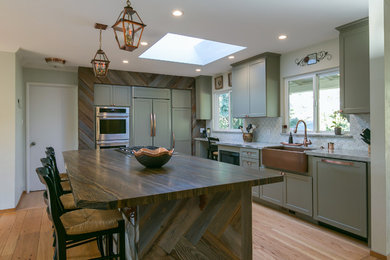 Inspiration for a mid-sized rustic l-shaped light wood floor and yellow floor open concept kitchen remodel in San Francisco with a farmhouse sink, shaker cabinets, green cabinets, quartzite countertops, multicolored backsplash, stainless steel appliances, an island and multicolored countertops