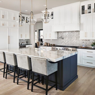 Inspiration for a transitional l-shaped medium tone wood floor and brown floor open concept kitchen remodel in Other with a farmhouse sink, shaker cabinets, white cabinets, subway tile backsplash, paneled appliances, an island and black countertops