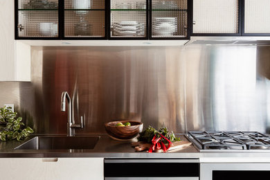 Cette image montre une petite cuisine américaine linéaire urbaine en bois clair avec un évier intégré, un placard à porte plane, un plan de travail en inox, un électroménager en acier inoxydable, sol en béton ciré, aucun îlot et un sol gris.
