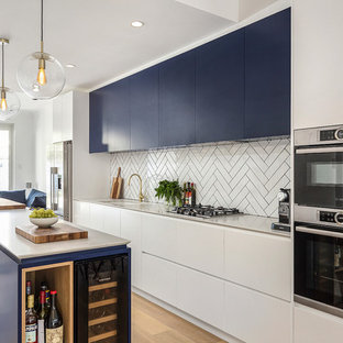 This is an example of a large contemporary galley open plan kitchen in Sydney with an undermount sink, flat-panel cabinets, blue cabinets, white splashback, subway tile splashback, light hardwood floors, with island, white benchtop, quartz benchtops, stainless steel appliances and brown floor.