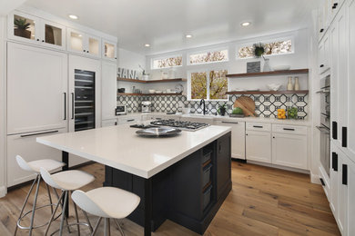Mid-sized minimalist u-shaped medium tone wood floor and brown floor eat-in kitchen photo in Orange County with a farmhouse sink, shaker cabinets, white cabinets, quartz countertops, multicolored backsplash, cement tile backsplash, paneled appliances, an island and white countertops