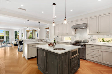 Example of a large transitional l-shaped medium tone wood floor enclosed kitchen design in Orange County with an undermount sink, shaker cabinets, beige cabinets, marble countertops, multicolored backsplash, stone tile backsplash, stainless steel appliances and an island