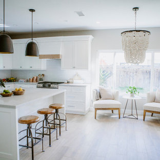 Photo of a mid-sized beach style l-shaped open plan kitchen in San Diego with an undermount sink, shaker cabinets, white cabinets, quartz benchtops, white splashback, subway tile splashback, stainless steel appliances, ceramic floors, with island and brown floor.