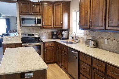 Example of a mid-sized classic l-shaped vinyl floor and beige floor kitchen pantry design in Little Rock with an undermount sink, raised-panel cabinets, medium tone wood cabinets, quartzite countertops, brown backsplash, porcelain backsplash, stainless steel appliances and an island