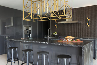 Cette image montre une cuisine design avec un évier encastré, un placard à porte plane, des portes de placard grises, une crédence marron, îlot, un sol beige et plan de travail noir.