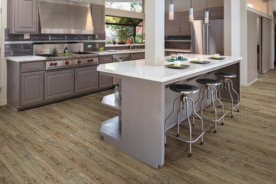 Inspiration for a mid-sized contemporary l-shaped dark wood floor and brown floor kitchen remodel in Miami with a double-bowl sink, raised-panel cabinets, gray cabinets, quartzite countertops, gray backsplash, subway tile backsplash, stainless steel appliances and an island