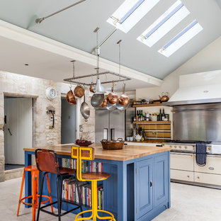Design ideas for a farmhouse kitchen in Gloucestershire with blue cabinets, wood worktops, an island, recessed-panel cabinets, white floors and white appliances.
