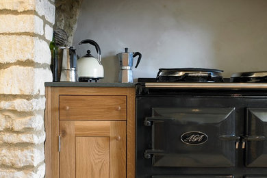 This is an example of a medium sized farmhouse l-shaped kitchen/diner in Gloucestershire with a belfast sink, flat-panel cabinets, medium wood cabinets, coloured appliances, limestone flooring and no island.