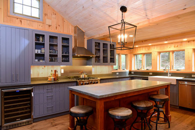 Example of a mid-sized farmhouse l-shaped medium tone wood floor and brown floor open concept kitchen design in Boston with a farmhouse sink, flat-panel cabinets, blue cabinets, granite countertops, gray backsplash, stone slab backsplash, stainless steel appliances, an island and gray countertops