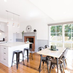 Inspiration for a scandinavian single-wall eat-in kitchen in Other with a farmhouse sink, shaker cabinets, white cabinets, white splashback, stainless steel appliances, medium hardwood floors, with island, brown floor and white benchtop.