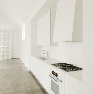 Mid-sized contemporary single-wall open plan kitchen in Houston with an undermount sink, flat-panel cabinets, white cabinets, white appliances, concrete floors, solid surface benchtops, no island and white splashback.
