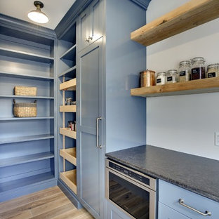 Design ideas for a mid-sized country l-shaped kitchen pantry in Minneapolis with a farmhouse sink, shaker cabinets, blue cabinets, quartzite benchtops, black splashback, subway tile splashback, panelled appliances, light hardwood floors and with island.