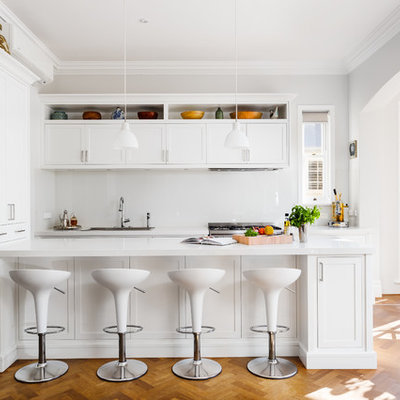 Example of a mid-sized transitional galley medium tone wood floor and brown floor kitchen design in Perth with white cabinets, solid surface countertops, glass sheet backsplash, stainless steel appliances, a drop-in sink, shaker cabinets and a peninsula