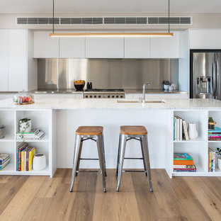 Photo of a contemporary single-wall open plan kitchen in Perth with flat-panel cabinets, white cabinets, marble benchtops, stainless steel appliances, with island, white benchtop, a double-bowl sink, metallic splashback, light hardwood floors and beige floor.