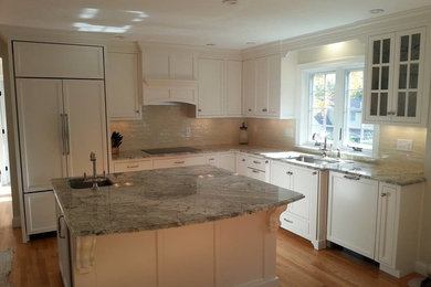 This is an example of a traditional kitchen in Boston with a submerged sink, granite worktops, black splashback, metro tiled splashback, integrated appliances, light hardwood flooring and an island.