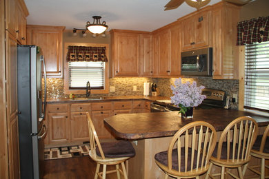 This is an example of a large farmhouse u-shaped kitchen/diner in Minneapolis with a submerged sink, raised-panel cabinets, light wood cabinets, laminate countertops, multi-coloured splashback, glass tiled splashback, stainless steel appliances, dark hardwood flooring and a breakfast bar.