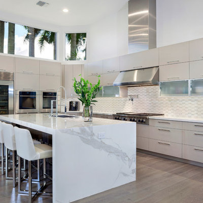 Example of a large trendy l-shaped medium tone wood floor eat-in kitchen design in Miami with an undermount sink, flat-panel cabinets, stainless steel appliances, an island, white cabinets, marble countertops, white backsplash and ceramic backsplash