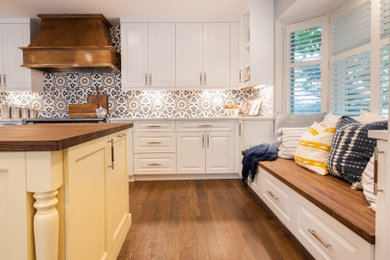 Example of a mid-sized transitional l-shaped dark wood floor enclosed kitchen design in Denver with a farmhouse sink, raised-panel cabinets, yellow cabinets, wood countertops, multicolored backsplash, porcelain backsplash, colored appliances, an island and brown countertops