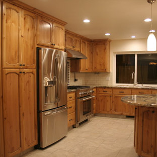 Cette image montre une cuisine américaine traditionnelle en U de taille moyenne avec un évier 3 bacs, un placard avec porte à panneau encastré, des portes de placard en bois brun, un plan de travail en granite, une crédence blanche, une crédence en carreau de céramique, un électroménager en acier inoxydable, un sol en carrelage de porcelaine et une péninsule.