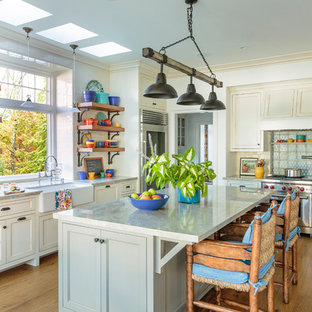 This is an example of a large beach style l-shaped kitchen in Los Angeles with a farmhouse sink, quartzite benchtops, white splashback, ceramic splashback, stainless steel appliances, with island, brown floor, recessed-panel cabinets, beige cabinets and dark hardwood floors.