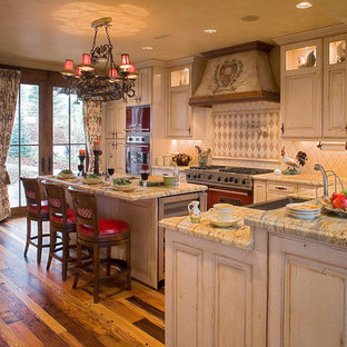 Idee per una cucina chic di medie dimensioni con ante con bugna sagomata, ante con finitura invecchiata, top in granito, paraspruzzi beige, paraspruzzi con piastrelle in pietra, lavello stile country, elettrodomestici in acciaio inossidabile, pavimento in legno massello medio, 2 o più isole e top multicolore