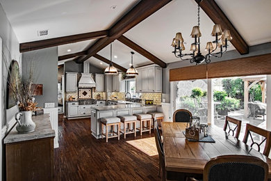 Photo of a large traditional u-shaped kitchen/diner in Orange County with a belfast sink, raised-panel cabinets, grey cabinets, engineered stone countertops, white splashback, metro tiled splashback, stainless steel appliances, dark hardwood flooring, a breakfast bar, brown floors and grey worktops.