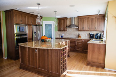 Inspiration for a mid-sized transitional medium tone wood floor eat-in kitchen remodel in Calgary with shaker cabinets, medium tone wood cabinets, granite countertops, beige backsplash, stone tile backsplash, an island, an undermount sink and stainless steel appliances