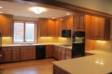 Enclosed kitchen - mid-sized traditional u-shaped light wood floor enclosed kitchen idea in Detroit with a double-bowl sink, raised-panel cabinets, brown cabinets, quartzite countertops, beige backsplash, ceramic backsplash, black appliances and a peninsula