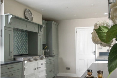 Large country l-shaped kitchen/diner in Sussex with a double-bowl sink, shaker cabinets, grey cabinets, granite worktops, green splashback, glass tiled splashback, white appliances, porcelain flooring, a breakfast bar and black worktops.