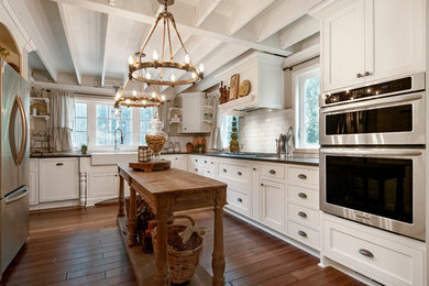 Eat-in kitchen - cottage u-shaped medium tone wood floor and brown floor eat-in kitchen idea in Seattle with a farmhouse sink, shaker cabinets, white cabinets, white backsplash, subway tile backsplash, stainless steel appliances, quartz countertops and an island