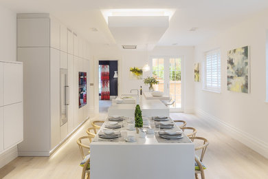 This is an example of a large contemporary open plan kitchen in Hampshire with flat-panel cabinets, yellow cabinets, composite countertops, black appliances, light hardwood flooring, an island, brown floors and yellow worktops.