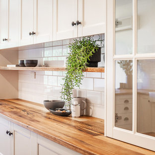 Immagine di una cucina country di medie dimensioni con lavello stile country, ante in stile shaker, ante bianche, top in legno, paraspruzzi bianco, paraspruzzi con piastrelle diamantate, elettrodomestici neri, pavimento in ardesia, penisola, pavimento grigio e top giallo