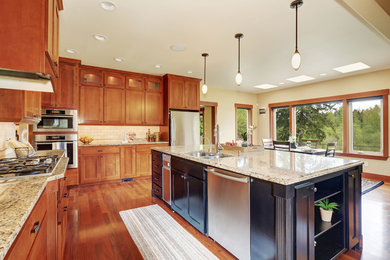 Example of a large mountain style l-shaped medium tone wood floor eat-in kitchen design in Los Angeles with a drop-in sink, shaker cabinets, light wood cabinets, granite countertops, brown backsplash, ceramic backsplash, stainless steel appliances and an island