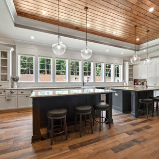 Large farmhouse u-shaped medium tone wood floor and brown floor kitchen photo in Atlanta with white cabinets, granite countertops, stainless steel appliances, two islands, a farmhouse sink, white backsplash, stone tile backsplash, gray countertops and shaker cabinets