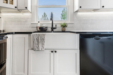 Small country u-shaped porcelain tile and beige floor eat-in kitchen photo in Other with a farmhouse sink, shaker cabinets, white cabinets, quartz countertops, white backsplash, subway tile backsplash, black appliances, a peninsula and black countertops