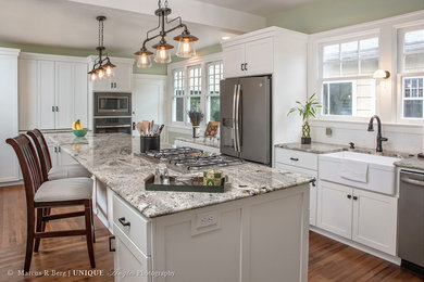 Large elegant galley medium tone wood floor eat-in kitchen photo in Portland with a farmhouse sink, shaker cabinets, white cabinets, white backsplash, ceramic backsplash, stainless steel appliances, an island and granite countertops