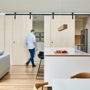 This is an example of a mid-sized contemporary galley open plan kitchen in Melbourne with flat-panel cabinets, white cabinets, marble benchtops, grey splashback, stone slab splashback, stainless steel appliances, light hardwood floors, with island, beige floor and white benchtop.