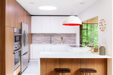 Inspiration for a midcentury u-shaped kitchen in Philadelphia with a submerged sink, flat-panel cabinets, composite countertops, grey splashback, porcelain splashback, stainless steel appliances, porcelain flooring, a breakfast bar, white cabinets and white floors.