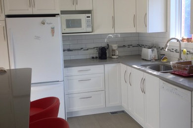 Enclosed kitchen - mid-sized contemporary l-shaped laminate floor and brown floor enclosed kitchen idea in Ottawa with shaker cabinets, white cabinets, quartz countertops, white backsplash, subway tile backsplash, white appliances, a double-bowl sink, gray countertops and a peninsula