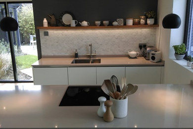 Small modern kitchen/diner in Buckinghamshire with a submerged sink, flat-panel cabinets, white cabinets, quartz worktops, beige splashback, porcelain splashback, integrated appliances, medium hardwood flooring and an island.