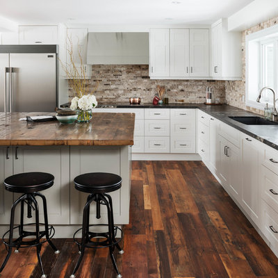 Open concept kitchen - large transitional l-shaped dark wood floor open concept kitchen idea in Toronto with white cabinets, an island, recessed-panel cabinets, beige backsplash, stone tile backsplash and stainless steel appliances
