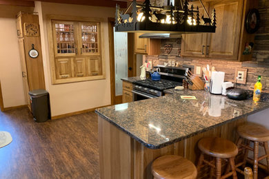 Cette image montre une cuisine américaine en bois brun avec un placard avec porte à panneau surélevé, un plan de travail en granite, un sol en vinyl, une péninsule, un sol marron et un plan de travail multicolore.