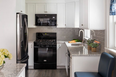 This is an example of a small traditional u-shaped kitchen/diner in Boston with a submerged sink, shaker cabinets, white cabinets, engineered stone countertops, grey splashback, metro tiled splashback, black appliances, laminate floors, an island, brown floors and multicoloured worktops.