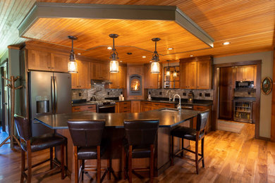 Open concept kitchen - large rustic l-shaped medium tone wood floor, brown floor and wood ceiling open concept kitchen idea in Burlington with an undermount sink, recessed-panel cabinets, medium tone wood cabinets, gray backsplash, stainless steel appliances, an island and gray countertops