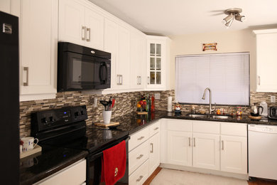 Example of a mid-sized transitional l-shaped medium tone wood floor kitchen pantry design in Miami with an undermount sink, recessed-panel cabinets, white cabinets, granite countertops, brown backsplash, glass tile backsplash, black appliances and no island
