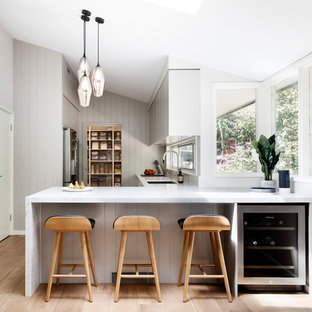 Inspiration for a large contemporary l-shaped eat-in kitchen in Sydney with an undermount sink, flat-panel cabinets, grey cabinets, quartz benchtops, window splashback, stainless steel appliances, medium hardwood floors, a peninsula, brown floor and white benchtop.