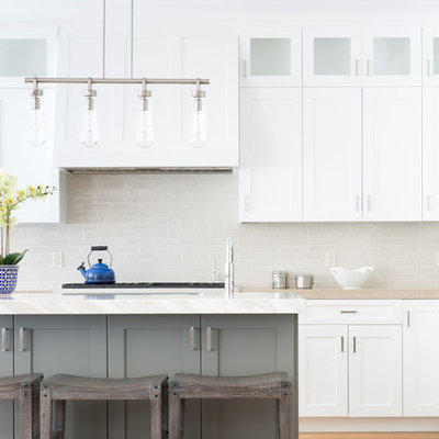 Example of a large transitional medium tone wood floor and beige floor eat-in kitchen design in San Francisco with a farmhouse sink, shaker cabinets, white cabinets, marble countertops, beige backsplash, ceramic backsplash, stainless steel appliances, an island and beige countertops